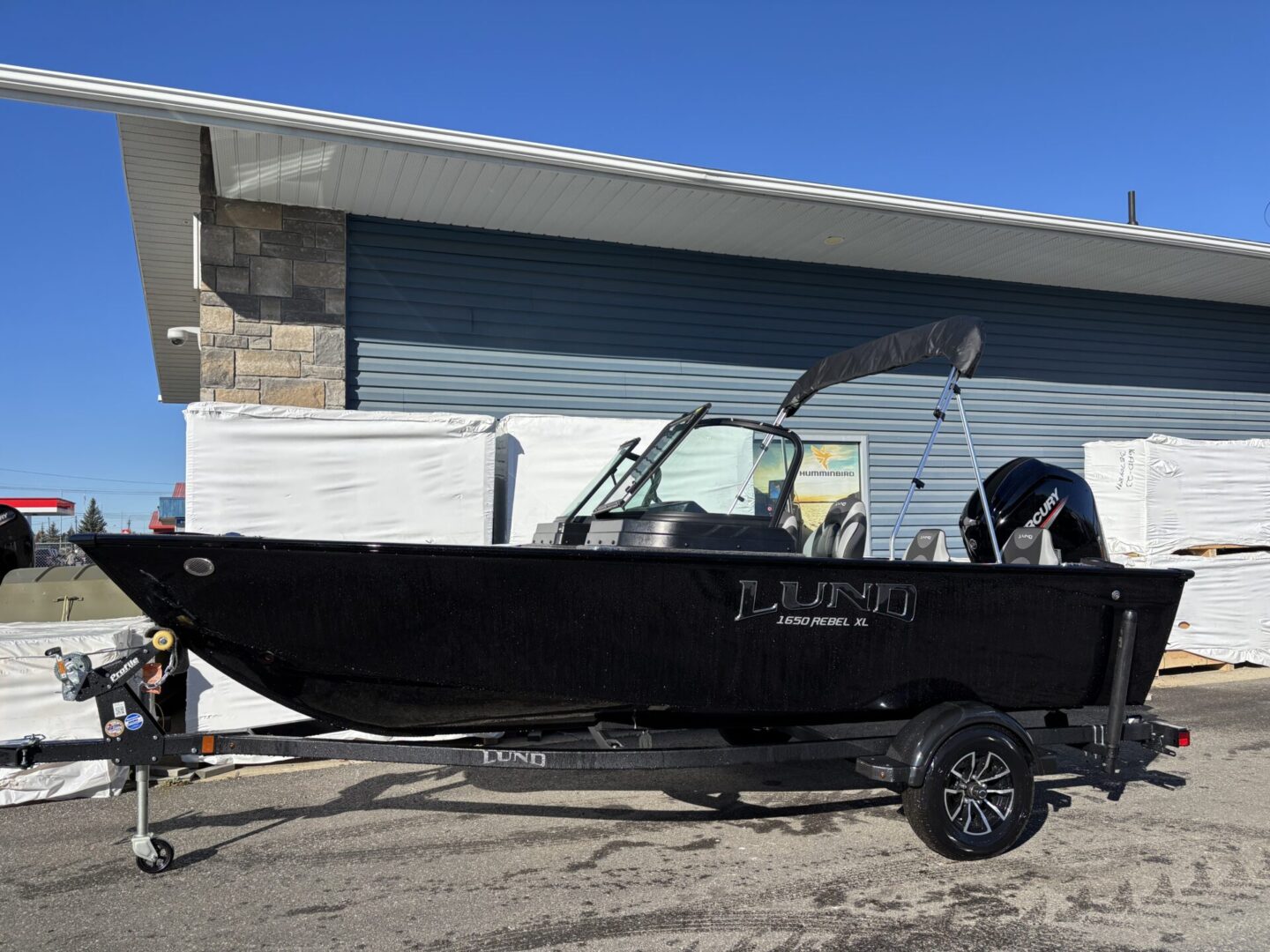 Black fishing boat on a trailer parked outside a building.