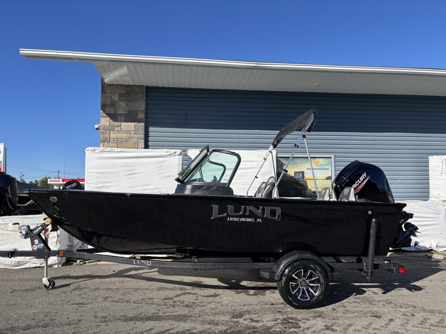 A black Lund boat parked on a trailer under a clear blue sky.