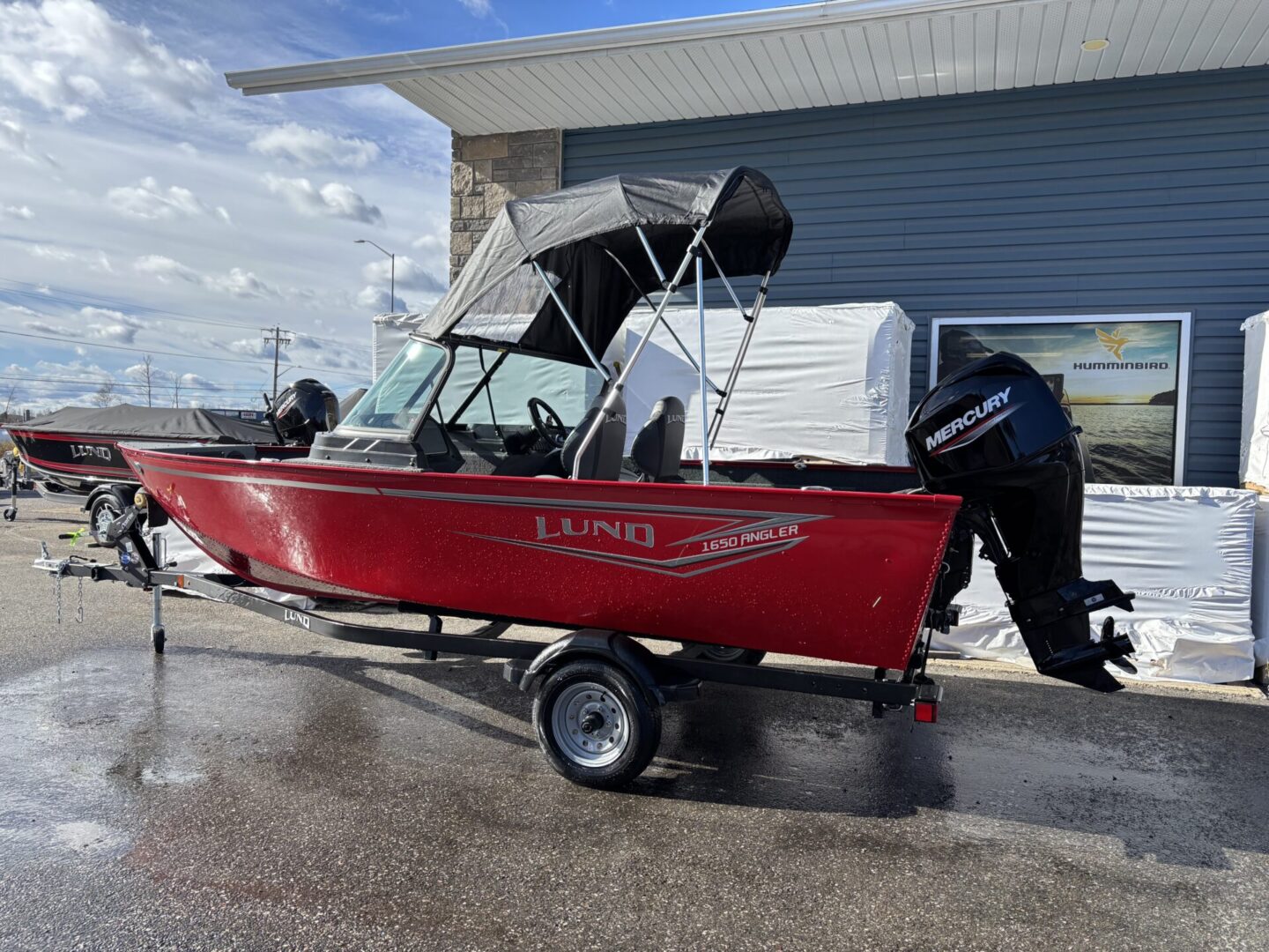 Red fishing boat with canopy on trailer near a building.