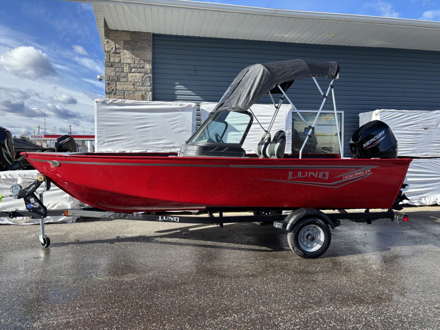 Red motorboat on a trailer parked outside a garage.