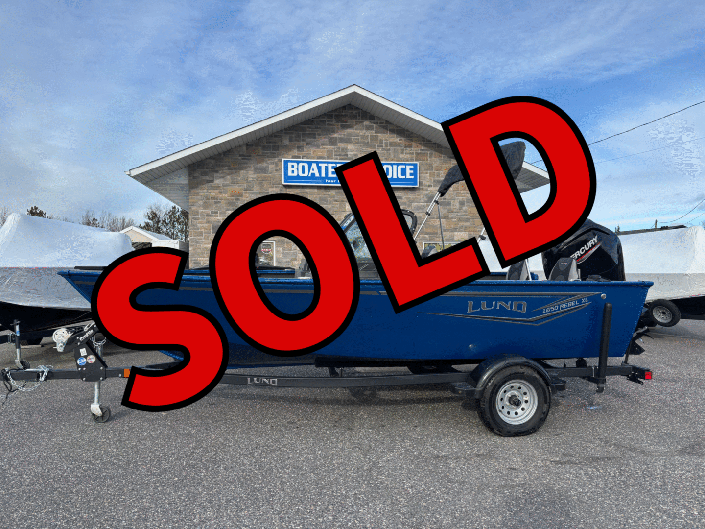 Blue boat on a trailer in front of a building with a SOLD sign.
