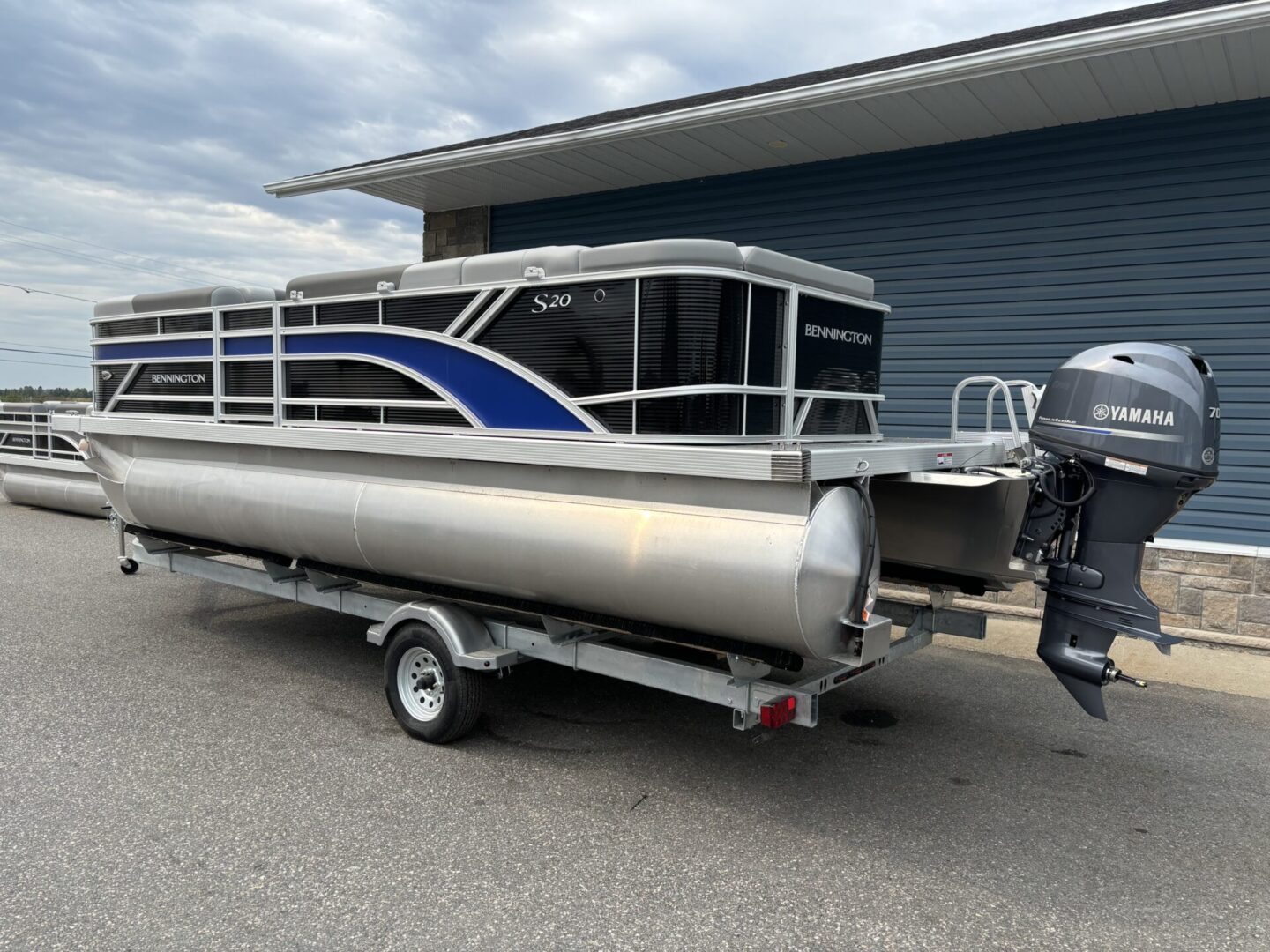 A pontoon boat with blue and black accents on a trailer near a building.
