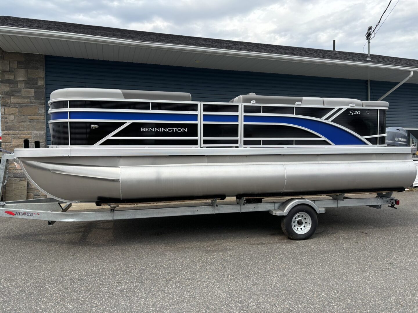 A blue and silver pontoon boat on a trailer in front of a building.