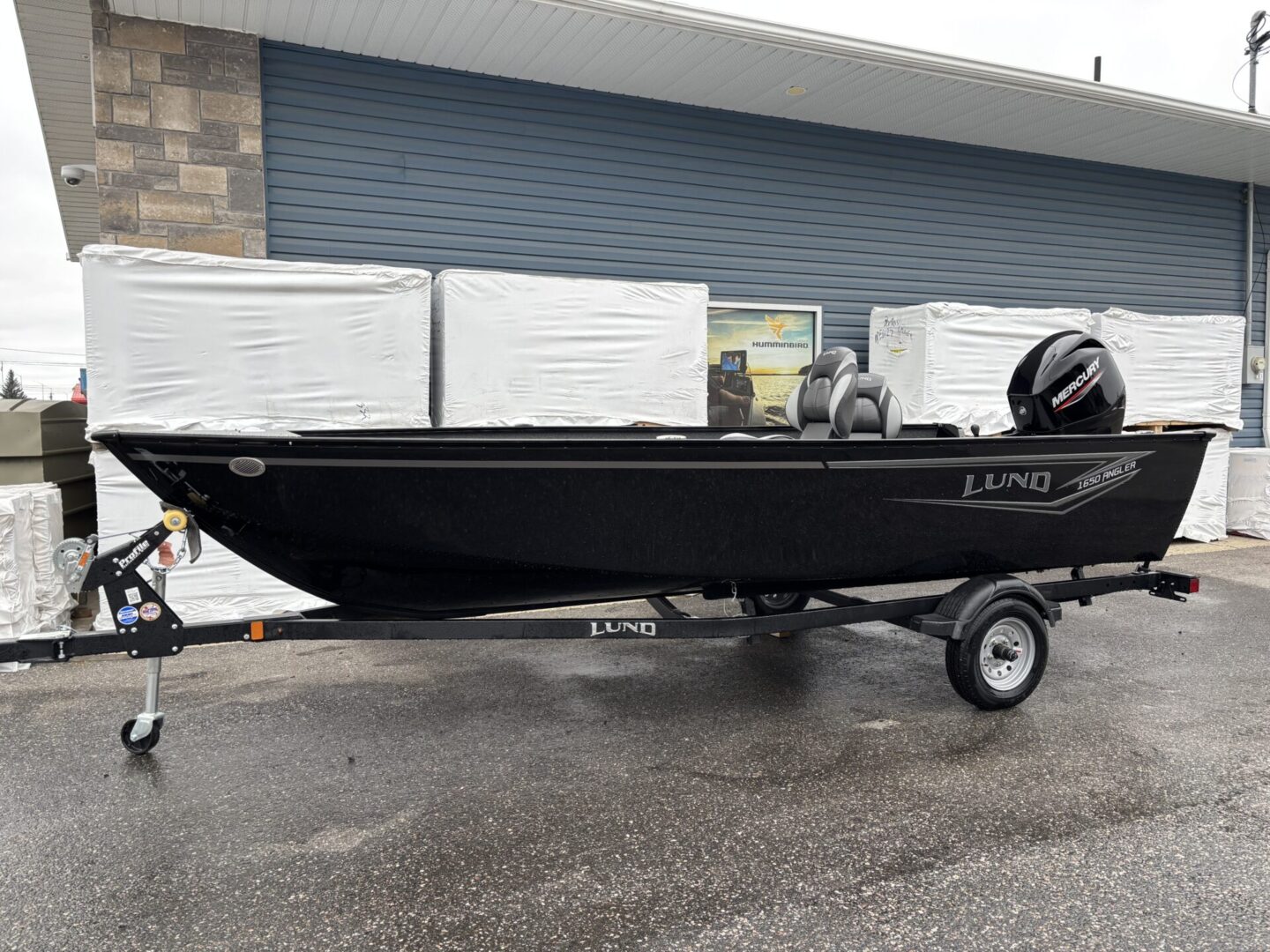 Black fishing boat on a trailer in a wet outdoor area.