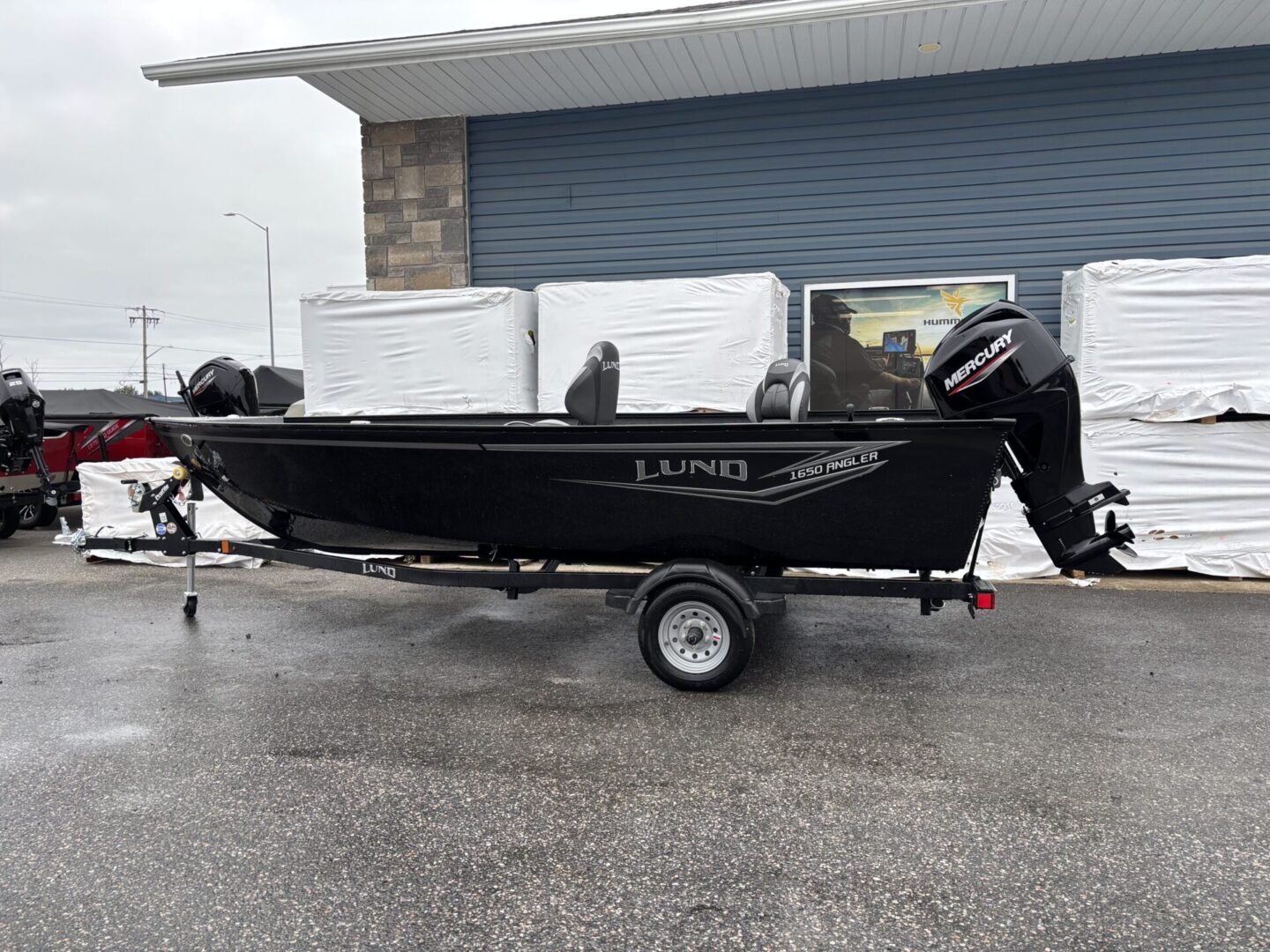 Black motorboat on a trailer parked outside on a rainy day.