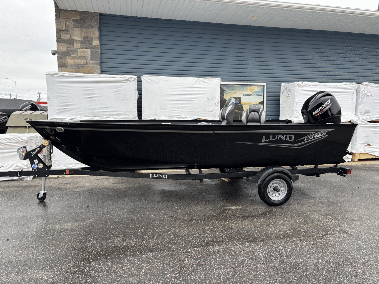A black Lund fishing boat on a trailer parked outdoors.