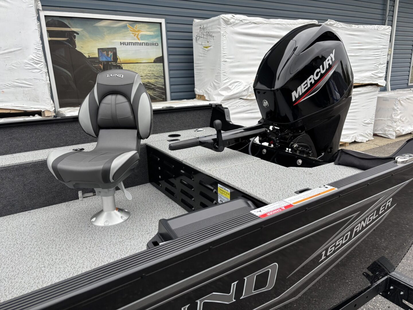 A sleek black fishing boat with a Mercury outboard motor docked near a lake.