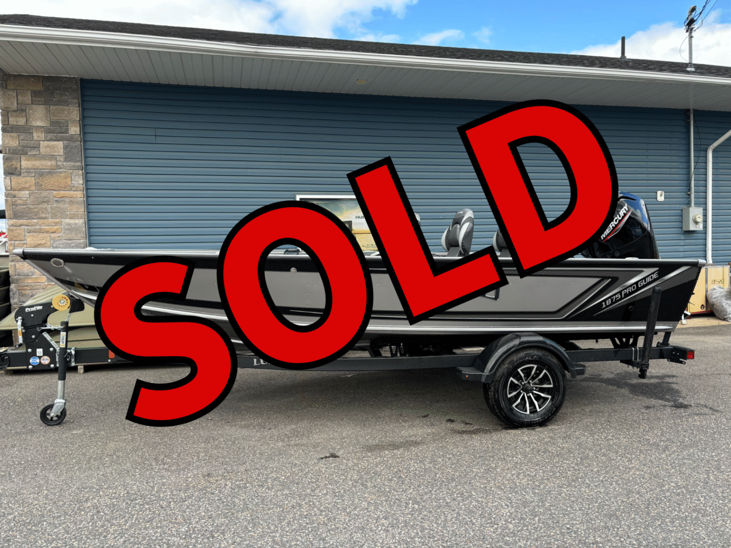 A black fishing boat with a 'SOLD' sign in front of a garage.