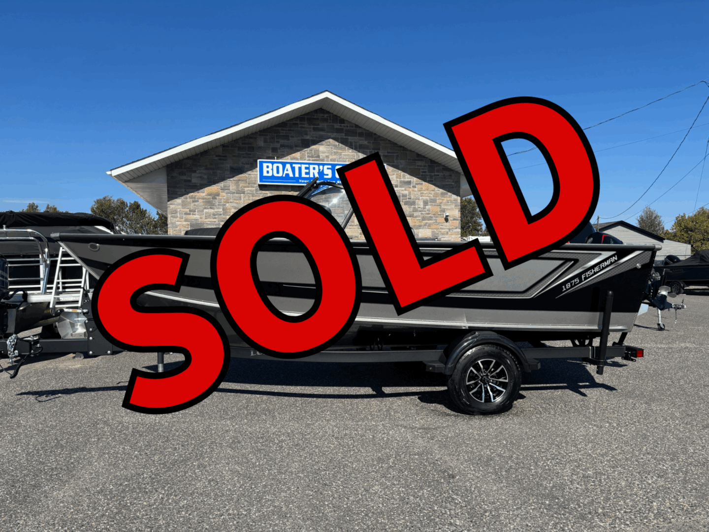 A black boat on a trailer in front of a building with a 'SOLD' text overlay.