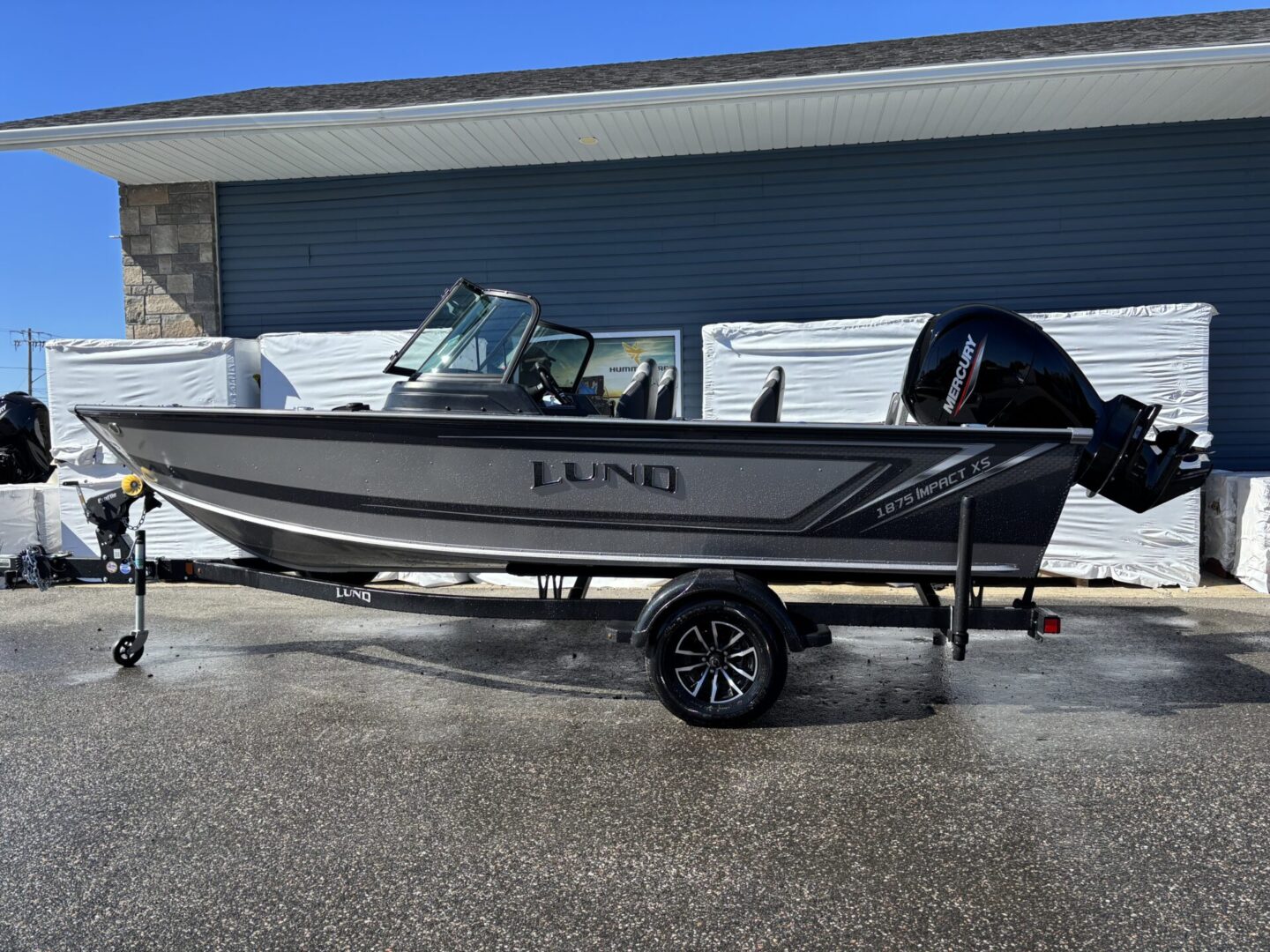 A small black fishing boat on a trailer in front of a garage.