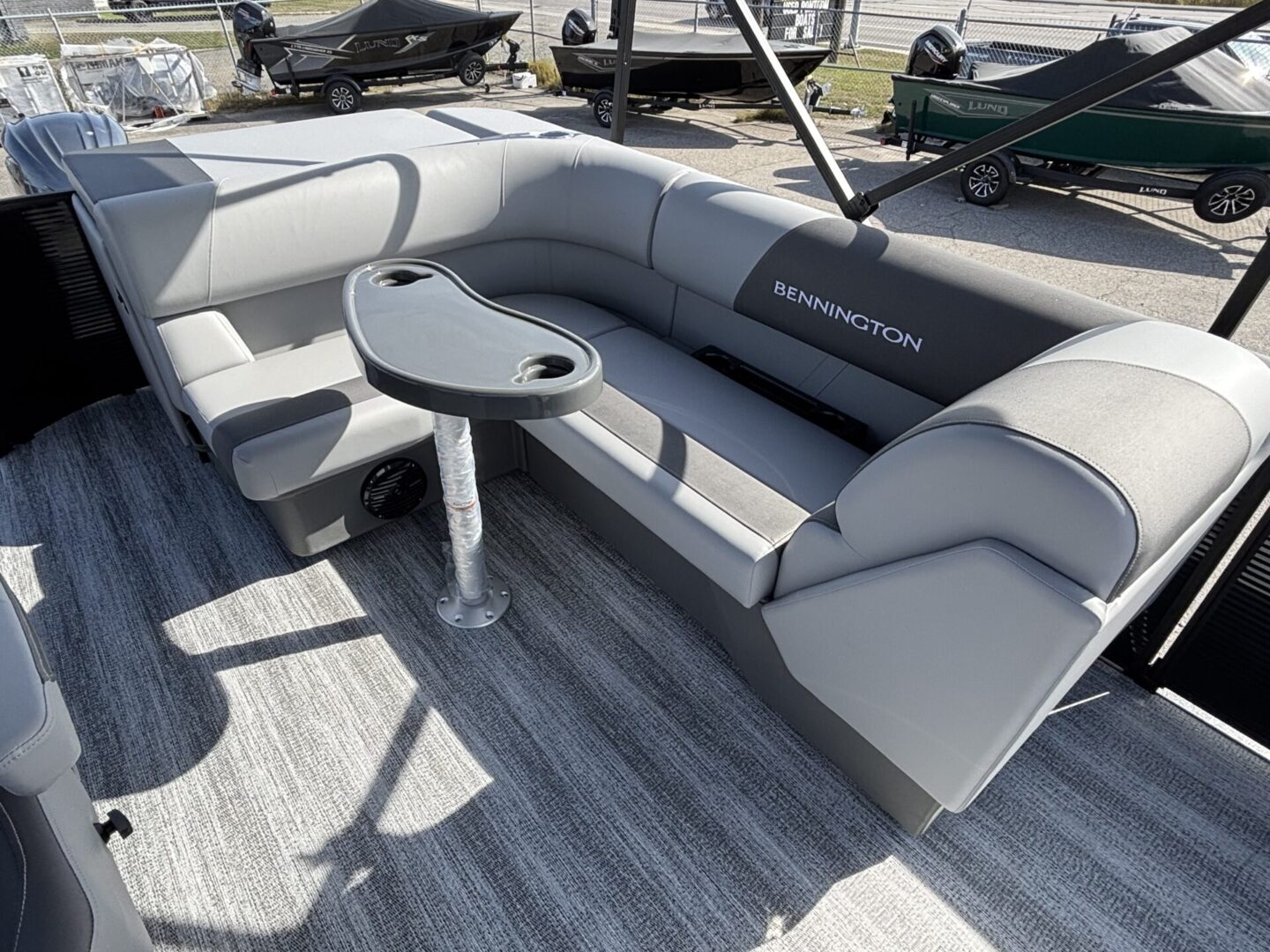 Spacious seating area on a modern pontoon boat with gray upholstery and a central table.
