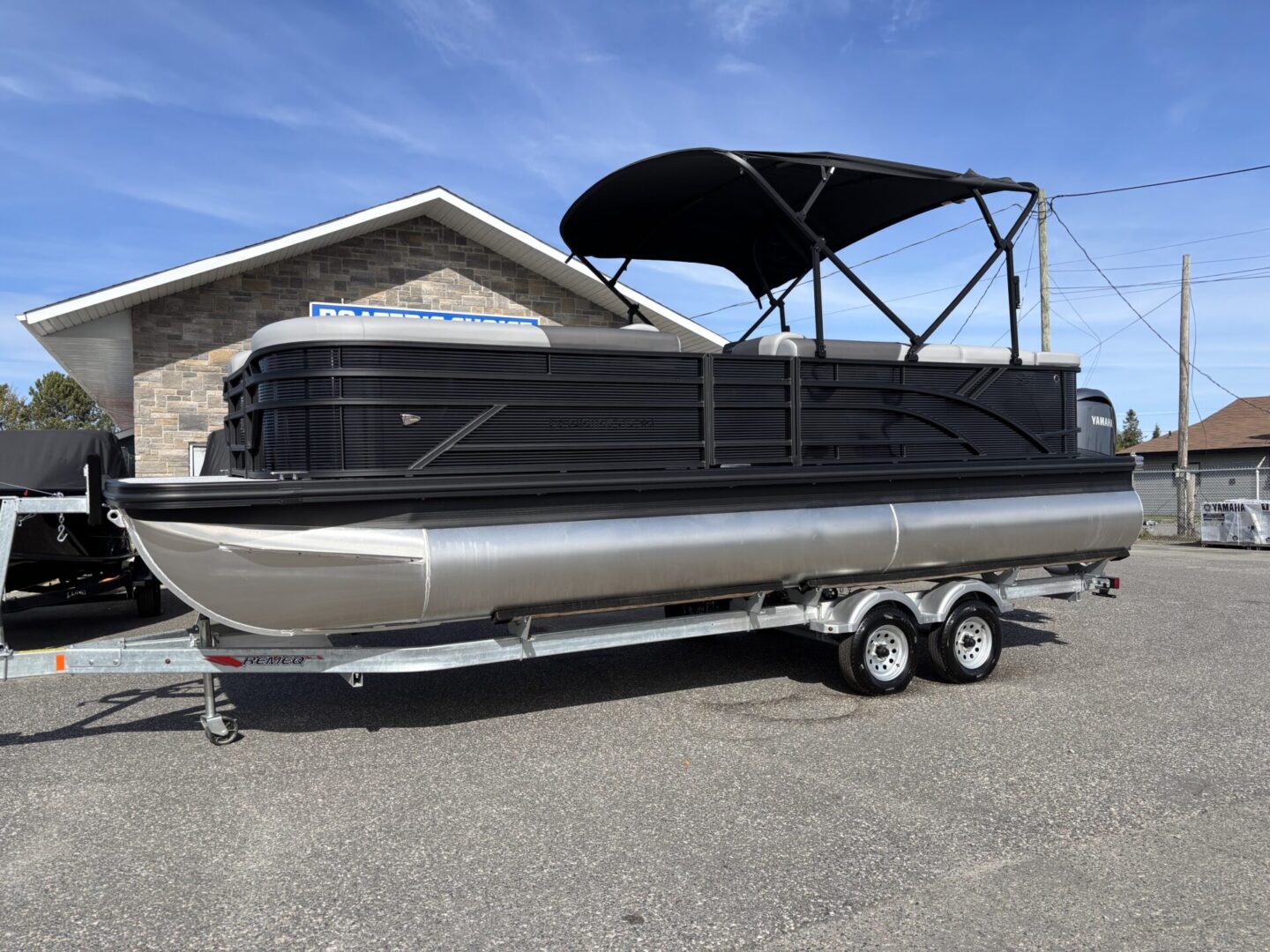 Black pontoon boat on a trailer under a clear sky.