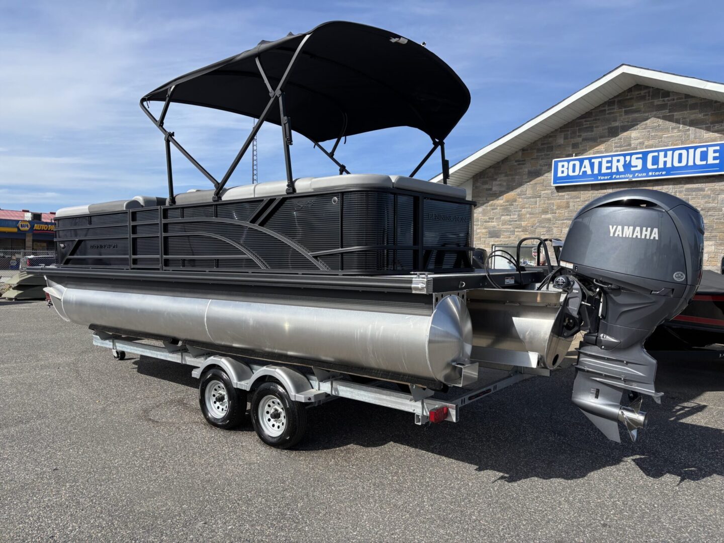 A sleek pontoon boat with a black canopy on a trailer under a clear sky.