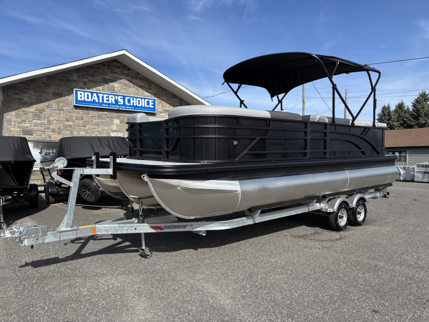 Black pontoon boat on a trailer outside a marina.
