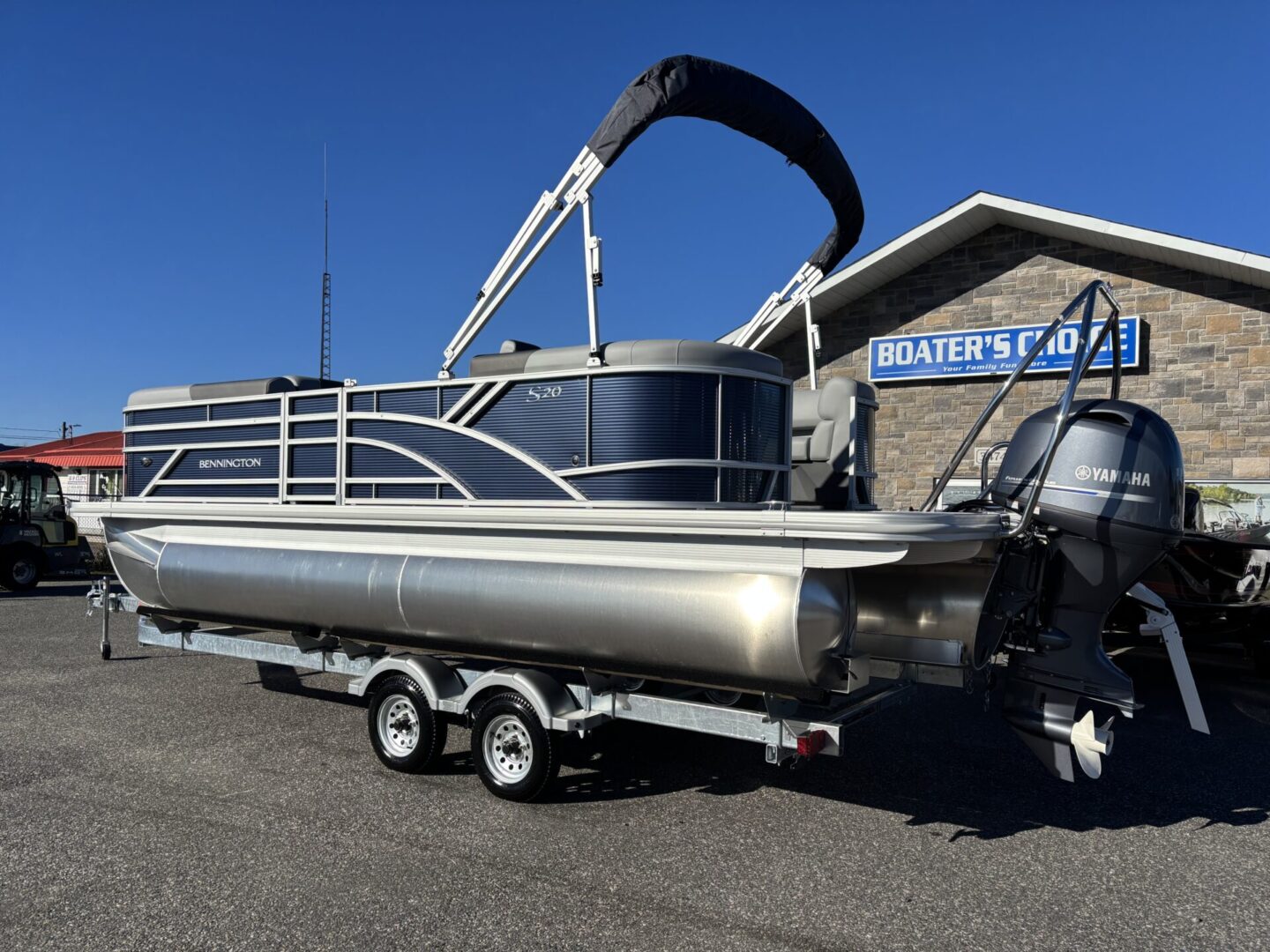Silver pontoon boat with black canopy on a triple-axle trailer under clear blue sky.