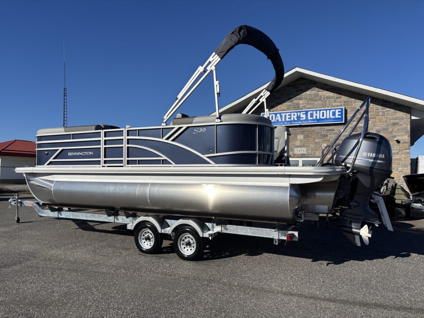 A sleek pontoon boat on a trailer parked outside a marine shop.
