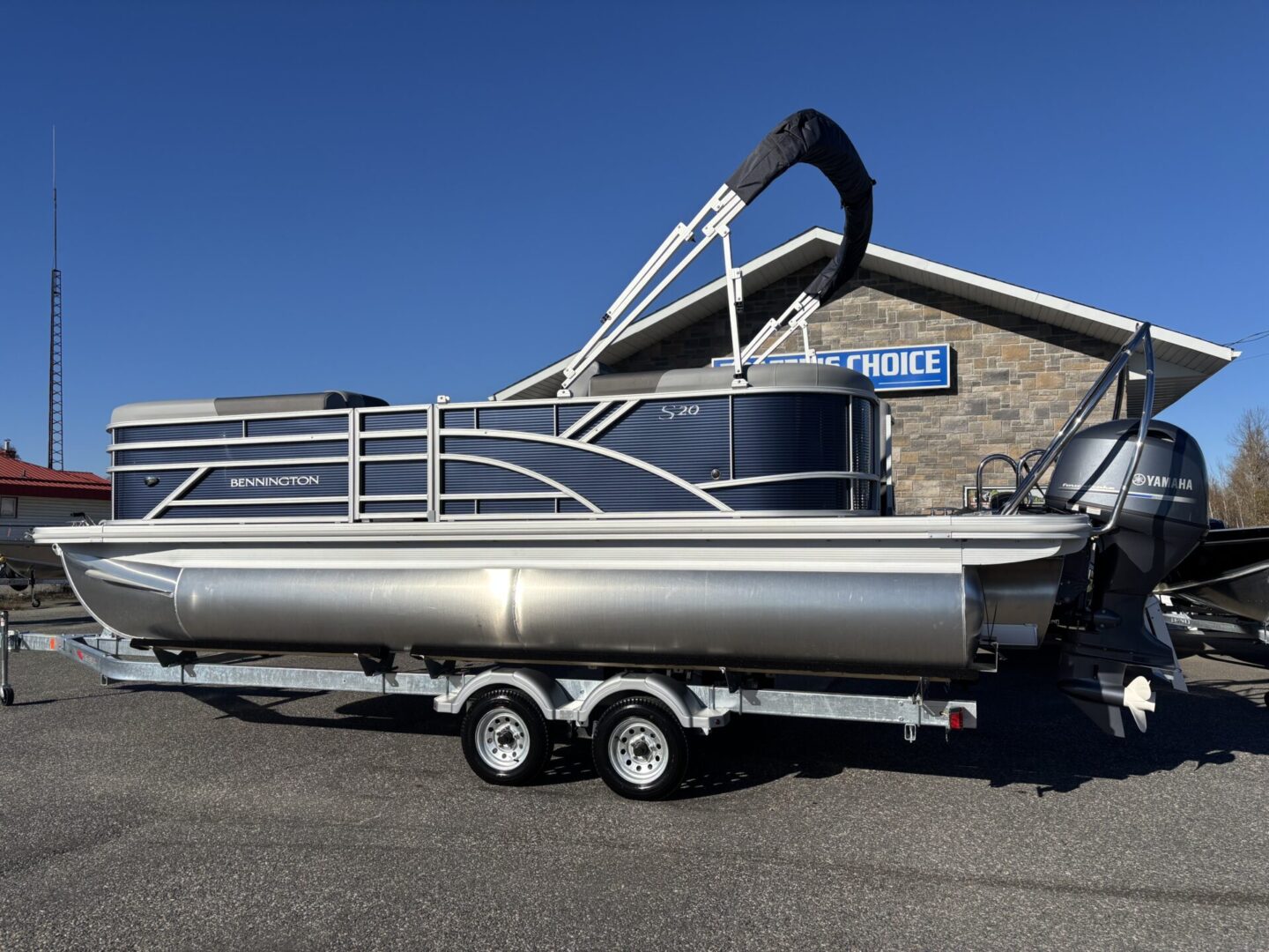 A silver pontoon boat on a trailer under a clear blue sky.