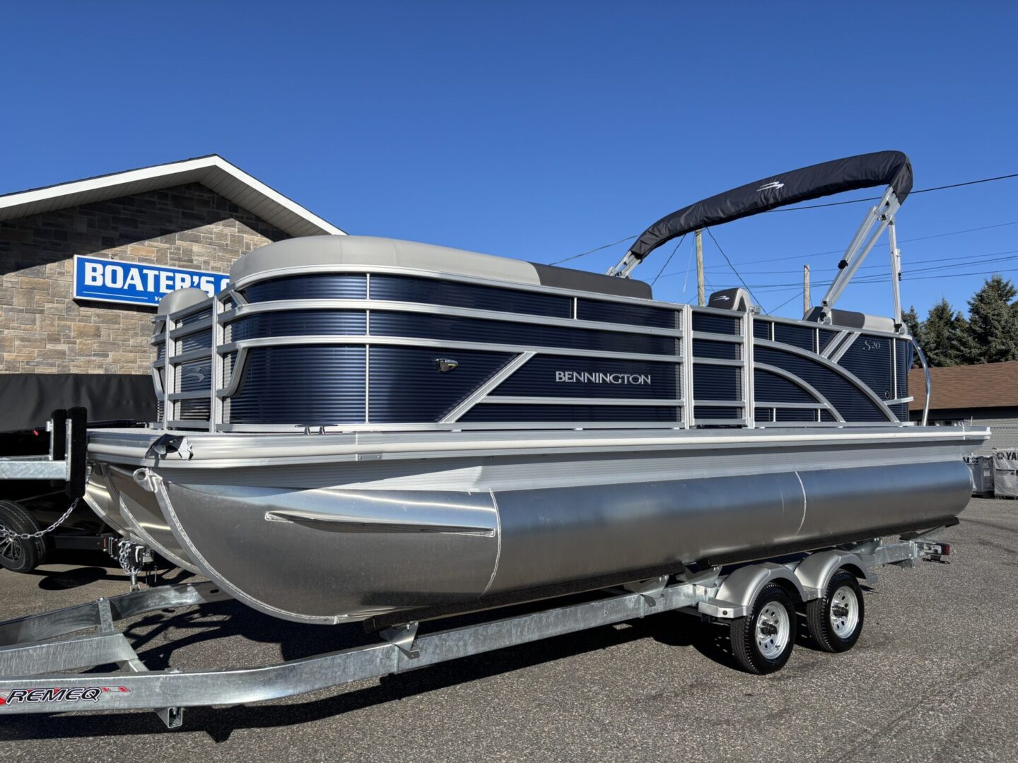 A sleek black and silver pontoon boat on a trailer under clear skies.