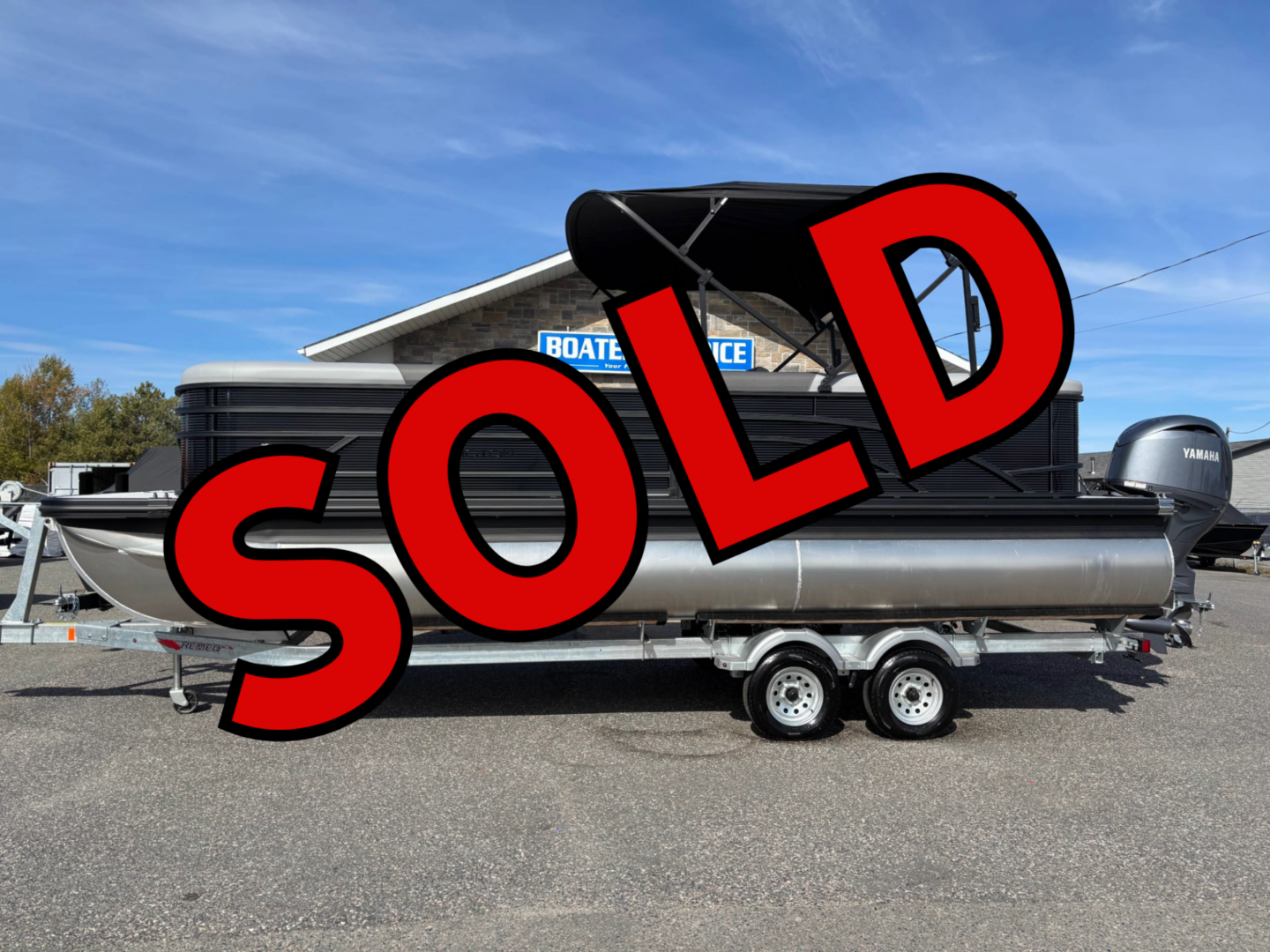 A pontoon boat with a 'SOLD' sign on it, parked on a trailer.