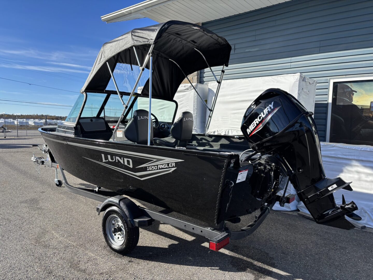 Black Lund motorboat on a trailer parked outside a house.