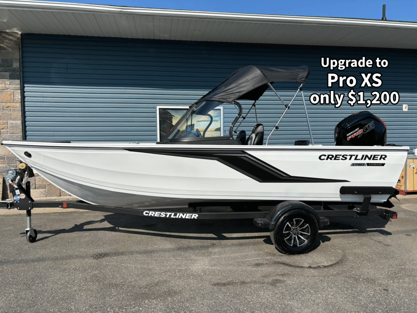 White and black Crestliner boat on trailer parked outside a blue building.
