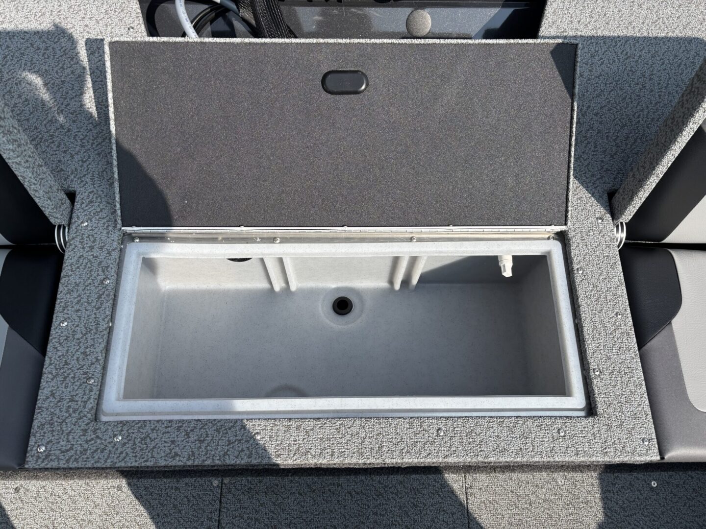 Open storage compartment with carpeted lid on outdoor surface.