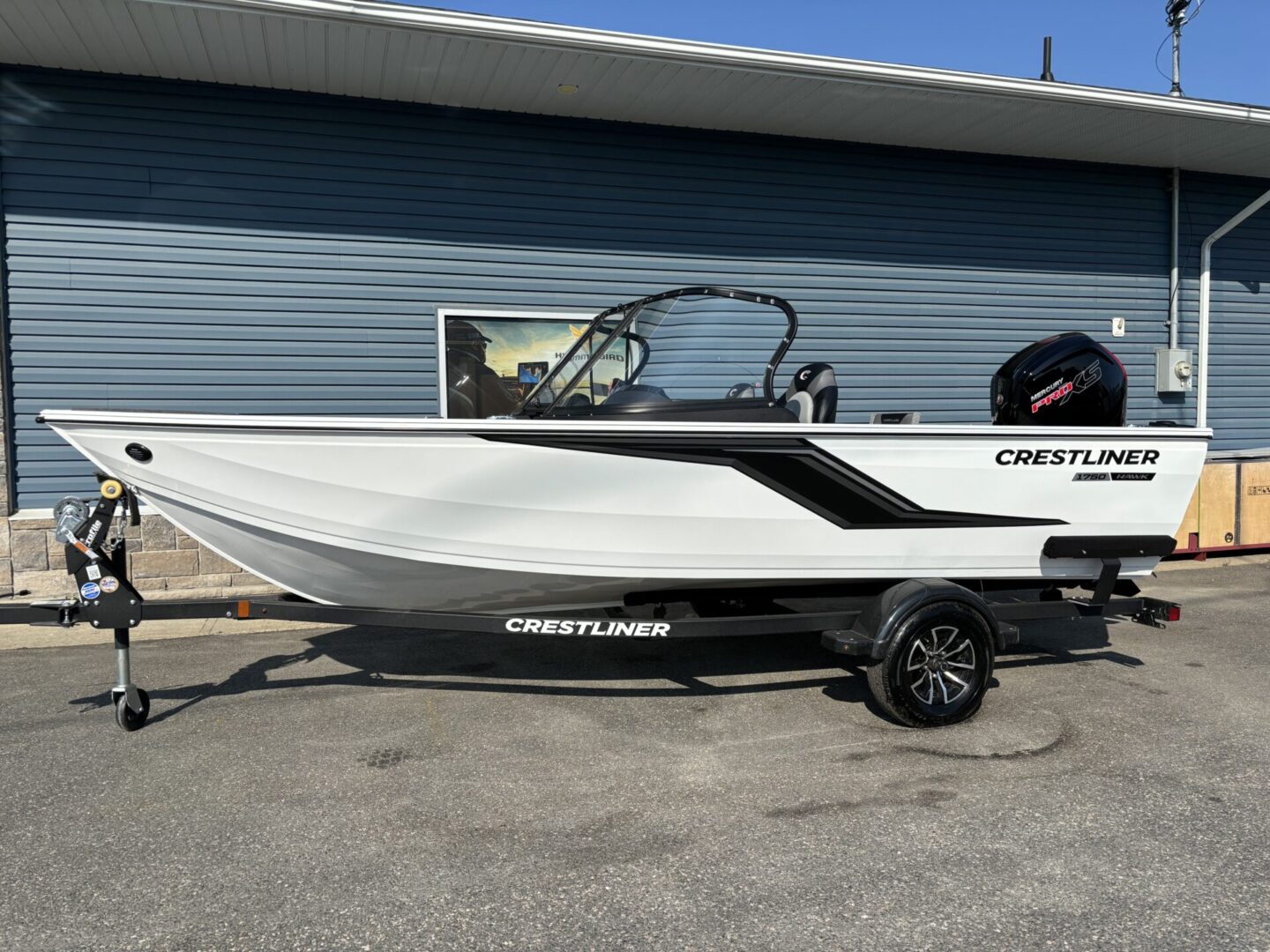 A sleek white and black Crestliner boat on a trailer under a clear blue sky.