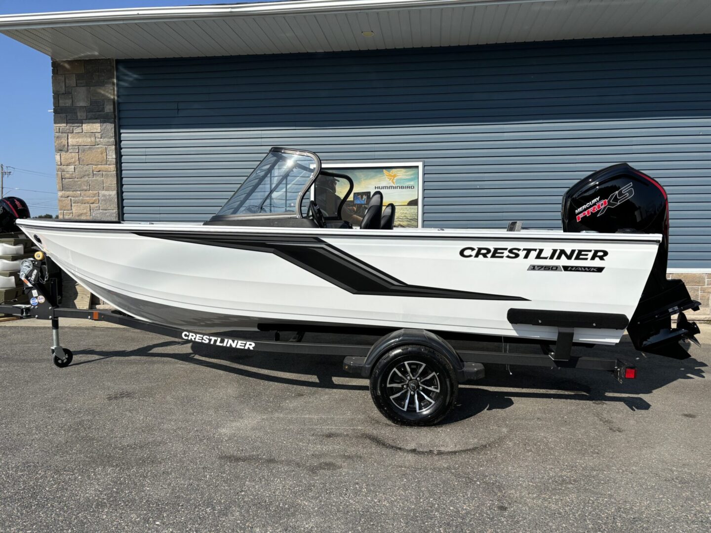 A sleek white Crestliner boat on a trailer, parked outside a building.