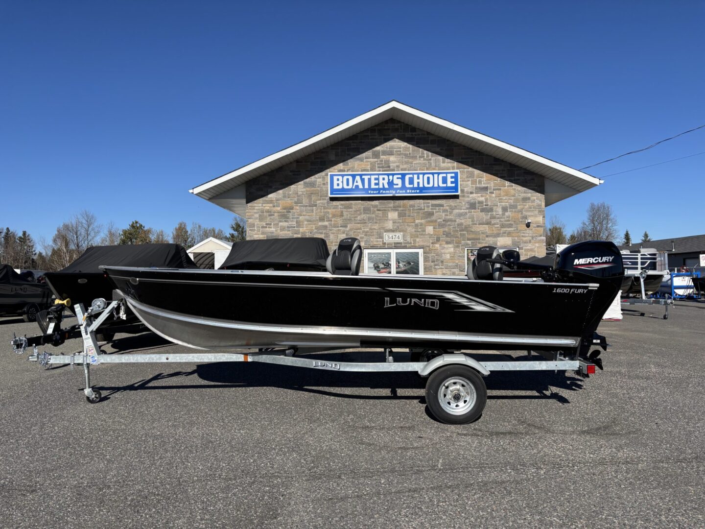 Black and silver fishing boat on a trailer in front of a building.
