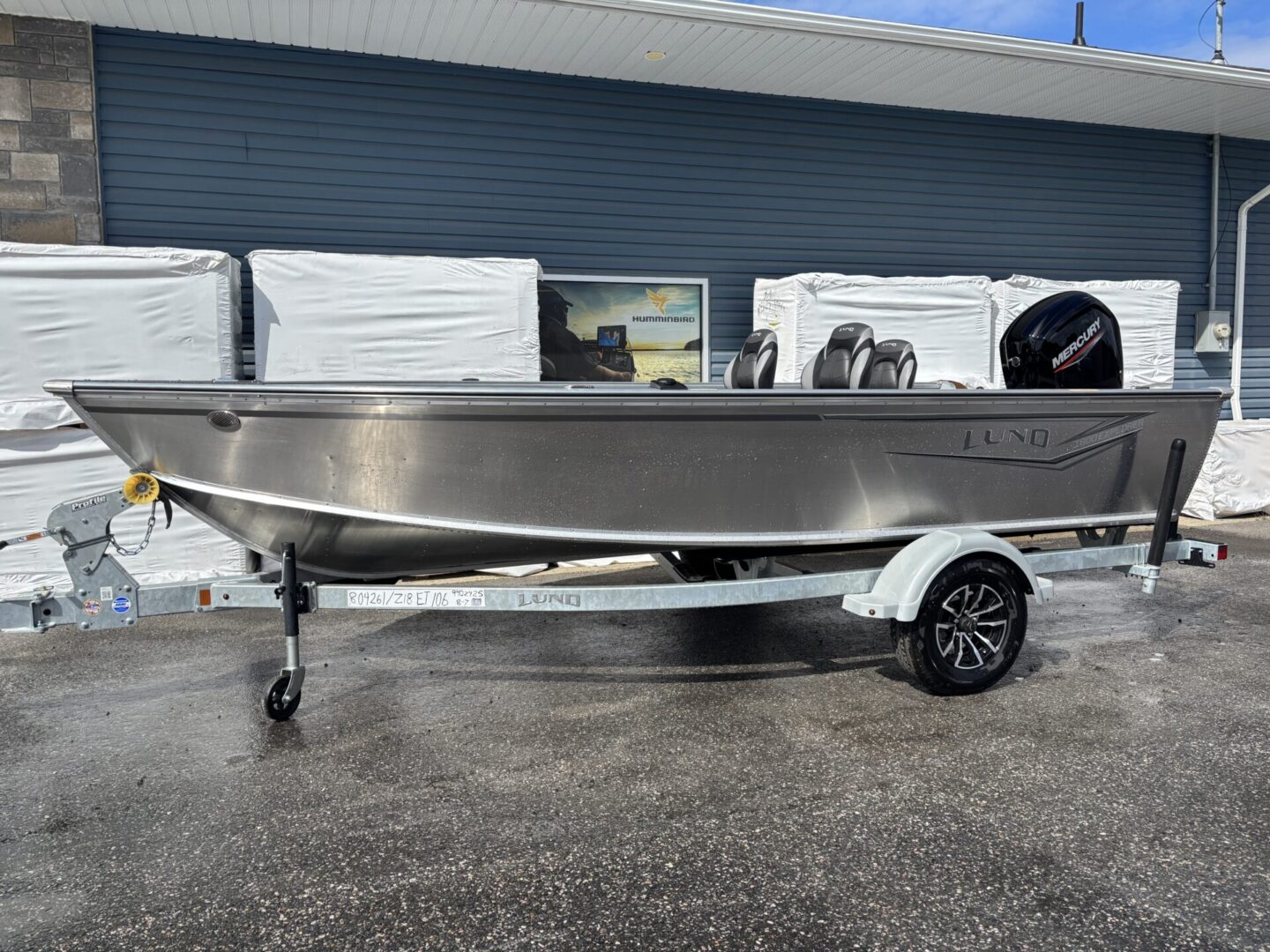 A sleek aluminum boat on a trailer outside a building under clear skies.