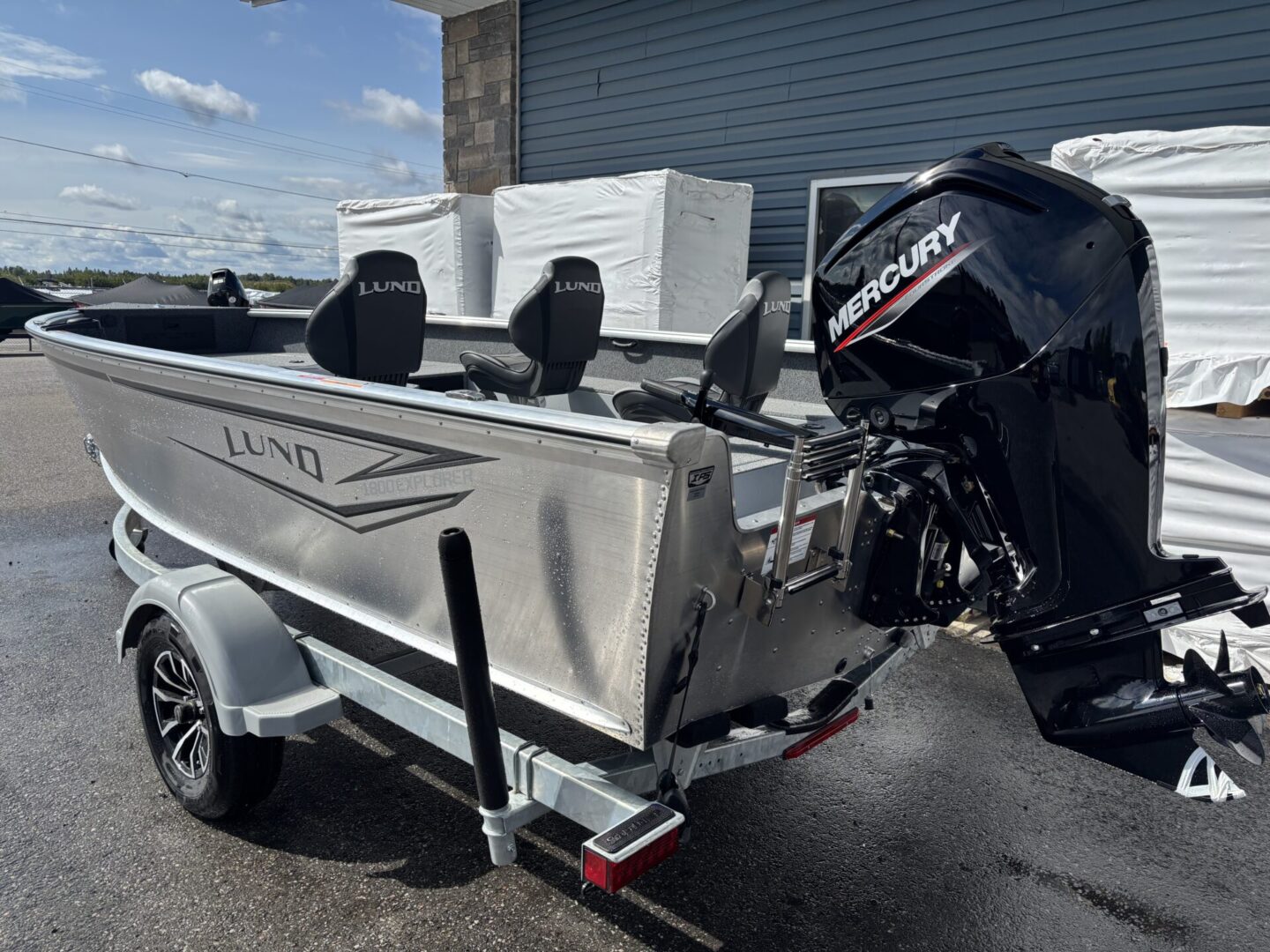 Silver fishing boat on trailer with Mercury outboard motor parked outdoors.