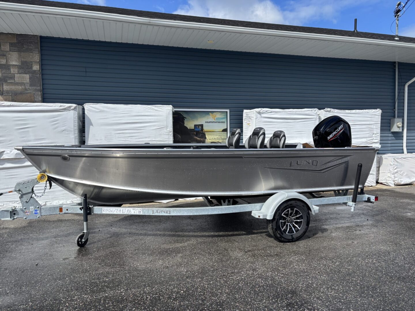 A shiny aluminum fishing boat on a trailer outside a building.