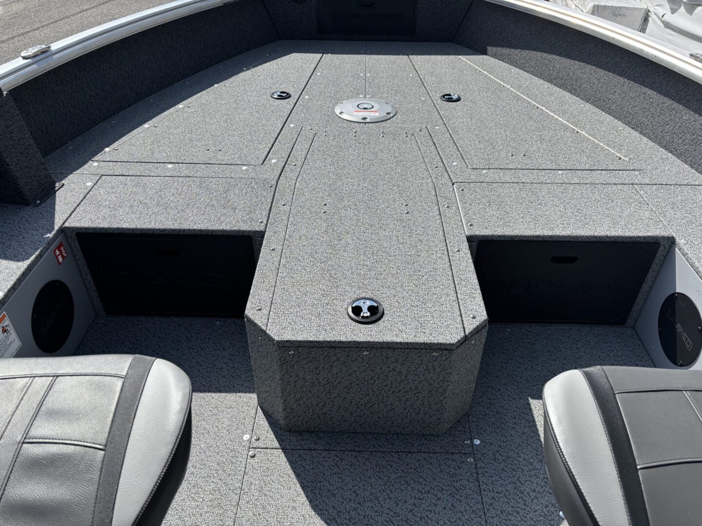 Front deck of a fishing boat with storage compartments and a textured gray surface.