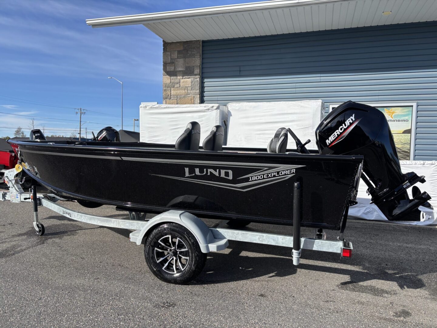 Black Lund fishing boat on a trailer parked near a building.