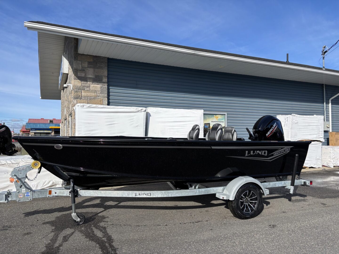 A black fishing boat on a trailer parked outside a building.