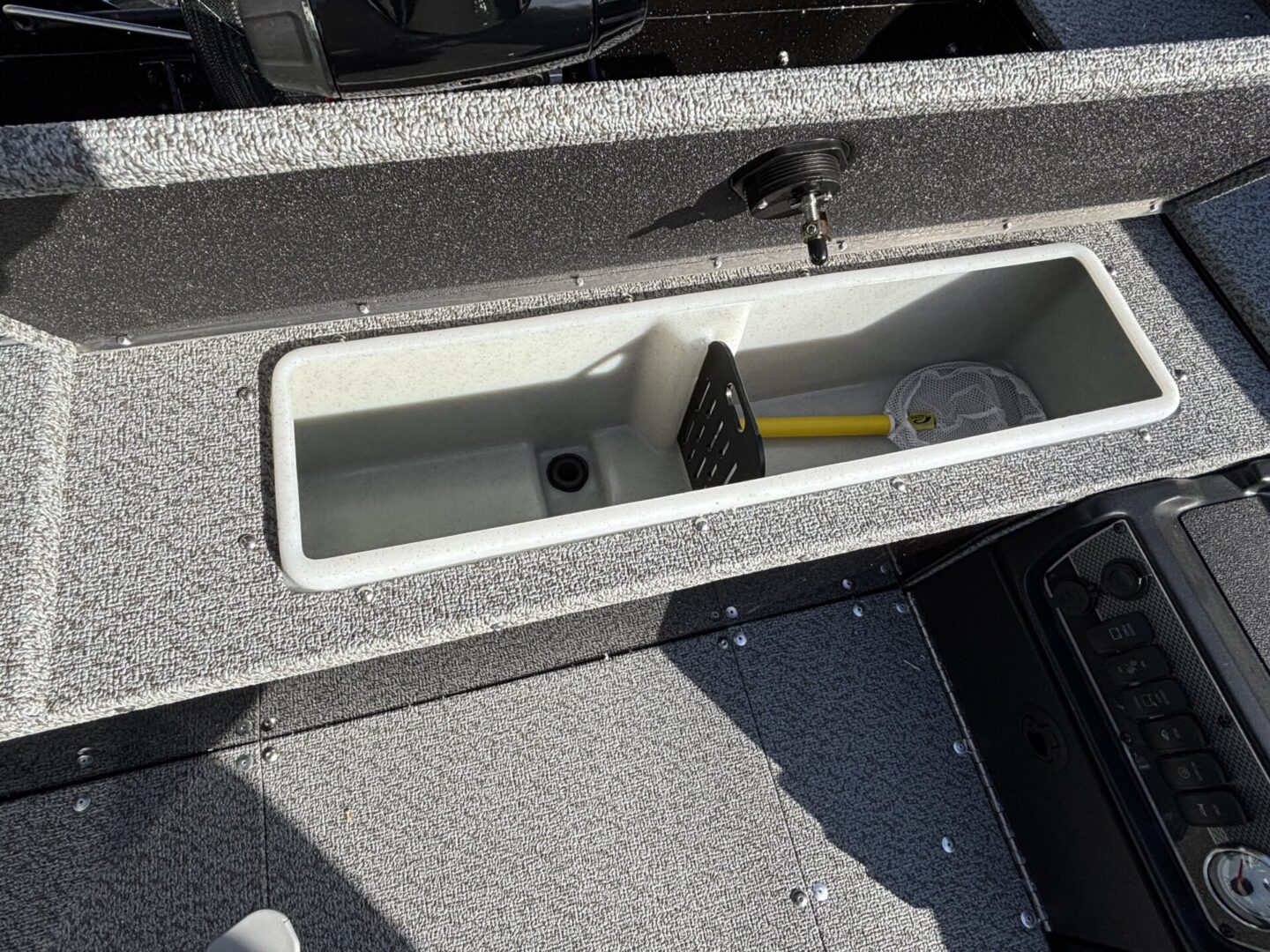 Open storage compartment with a yellow-handled tool inside on a boat deck.