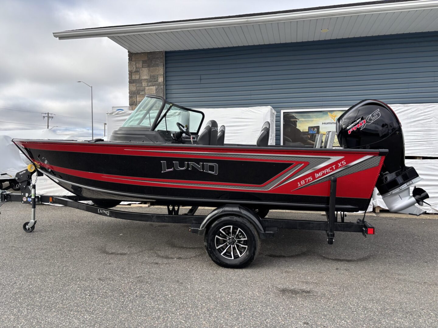 A red and black Lund fishing boat on a trailer parked outside a garage.