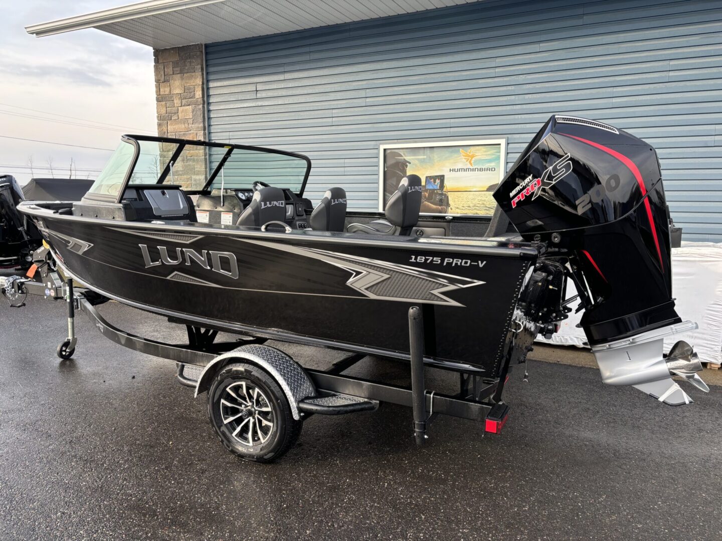 Black Lund fishing boat on trailer with outboard motor, parked indoors.