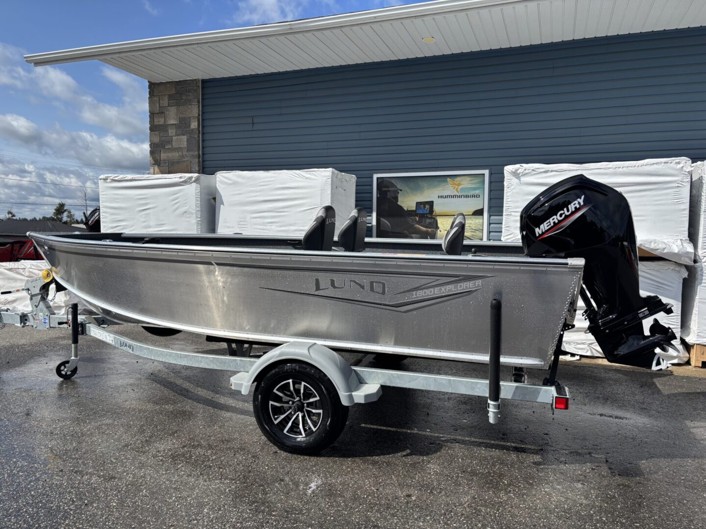 A sleek aluminum fishing boat on a trailer beside a garage.