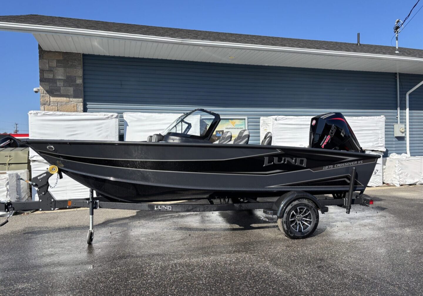 Black fishing boat with trailer parked outside a building.