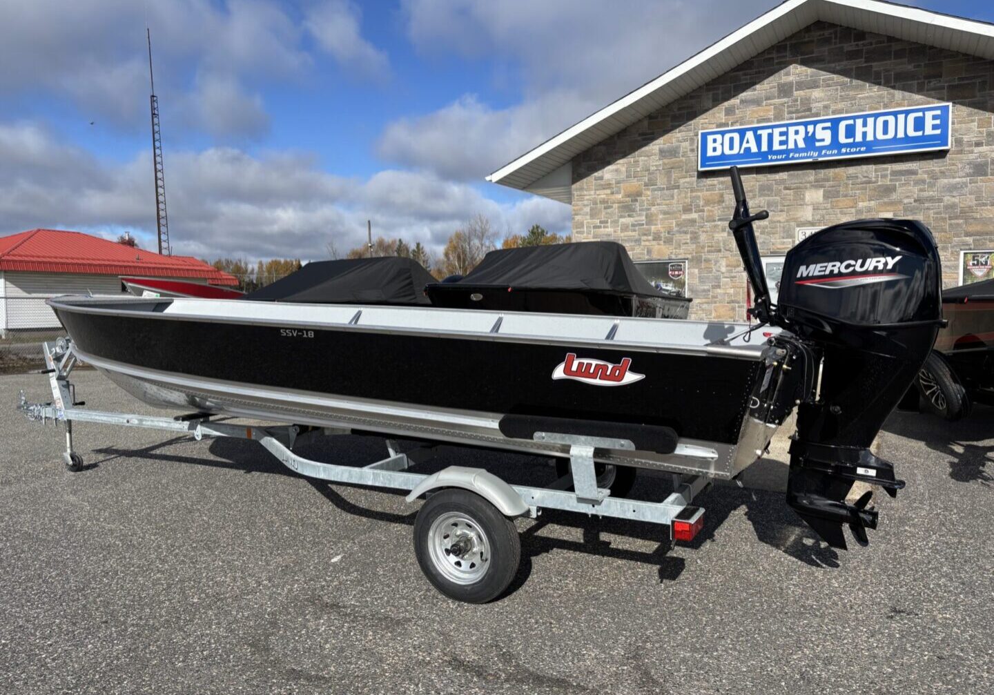 Black and red fishing boat on trailer under partly cloudy sky.
