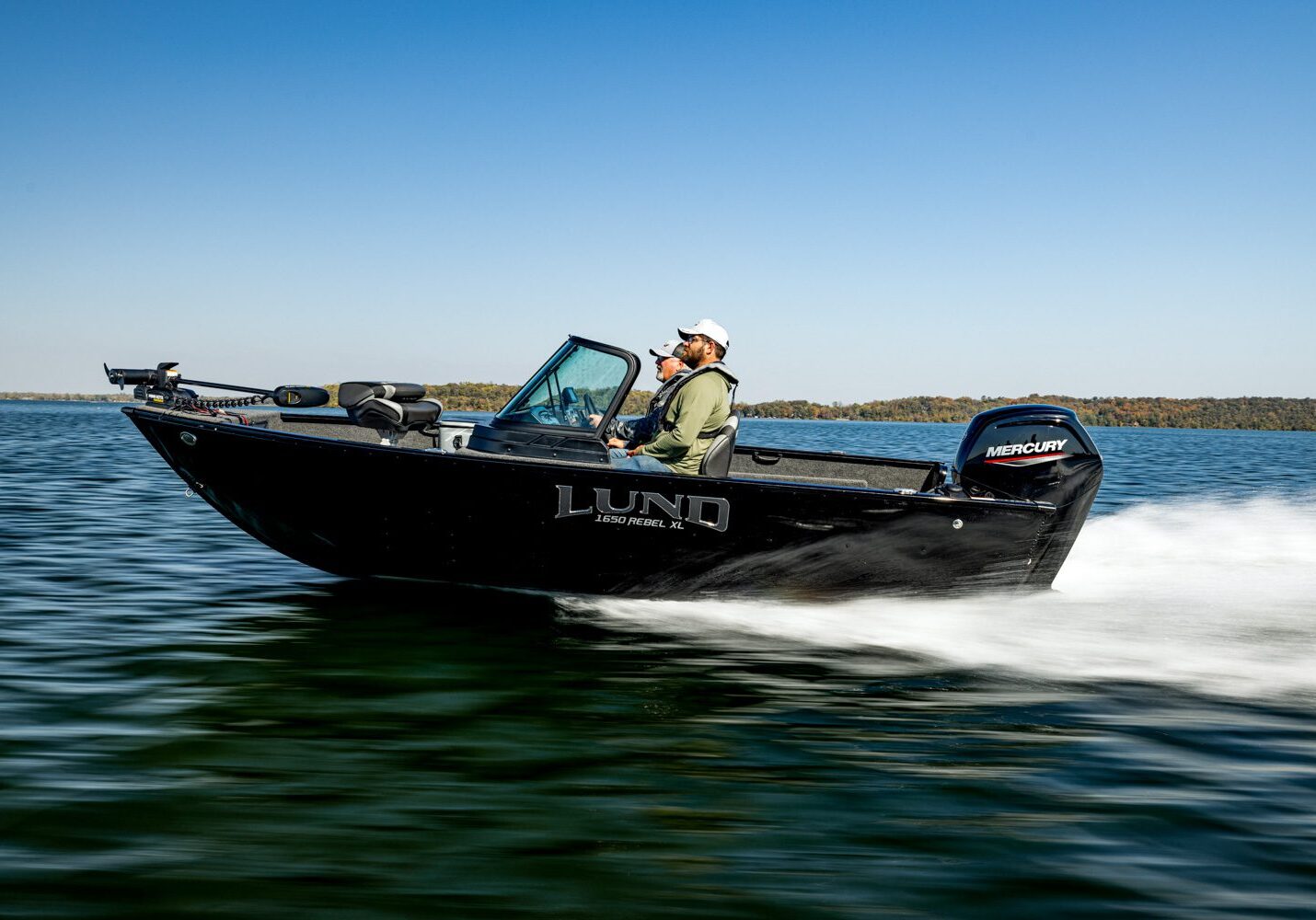 Man fishing on a black motorboat in calm waters under clear blue sky.